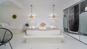 A modern bedroom with a large bed, bedside tables, a chair, and a glass-enclosed walk-in closet.