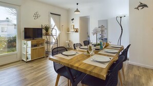 A modern dining area with a wooden table set for four, surrounded by black chairs. A television is mounted on the wall to the left, and there is a small plant on a shelf. - Bourg d'Olonne s/Mer, charming house for 6 people (Les Sables-d´Olonne)