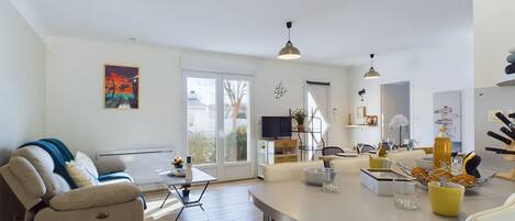 Un grand espace de vie comprenant un canapé, une table à manger et un coin cuisine à l’arrière-plan.