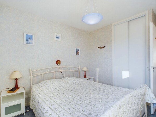 A bedroom with a bed, bedside tables, a nightstand, a hanging light fixture, and a door.