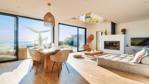 A spacious living area with a large window, a dining table with chairs, a sofa, and a fireplace. - Pool, view and beach access, 6 adults/2 children (La Guérinière)