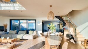 A spacious living room with a large sofa, a dining table set for six, and a staircase leading to an upper level. - Pool, view and beach access, 6 adults/2 children (La Guérinière)