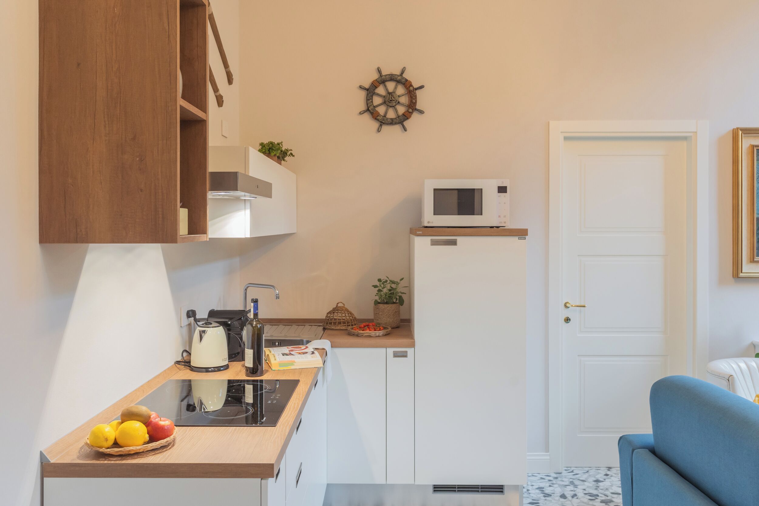 Eine kleine Küche mit Mikrowelle, Wasserkocher und Obstschale. Über der Arbeitsfläche befindet sich ein Holzschrank und im Hintergrund eine weiße Tür.