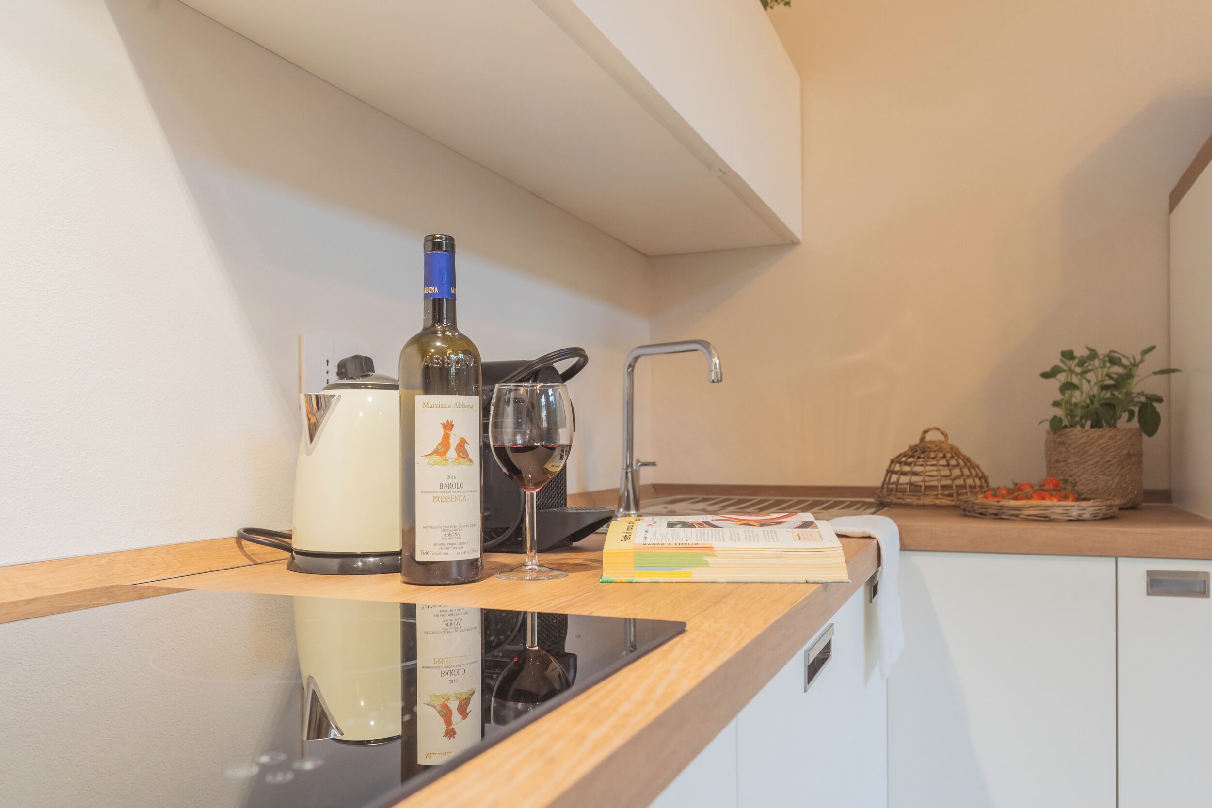 A kitchen counter with a wine bottle, a wine glass, a kettle, and a cookbook.