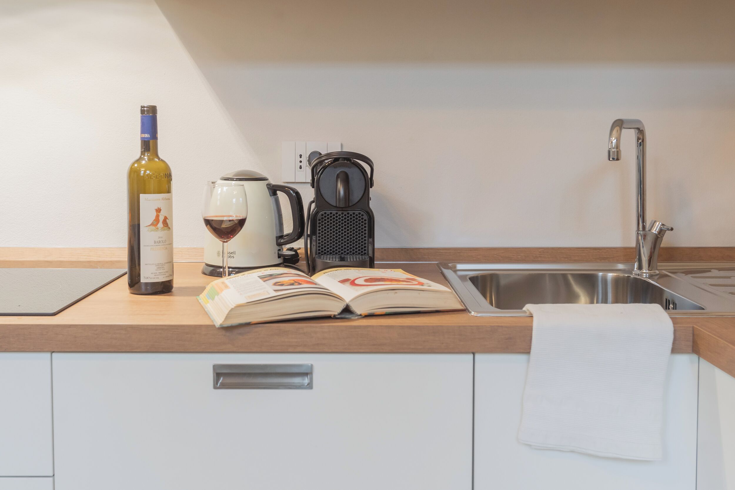 Un piano di lavoro in cucina con una bottiglia di vino, una macchina per il caffè e un libro aperto.