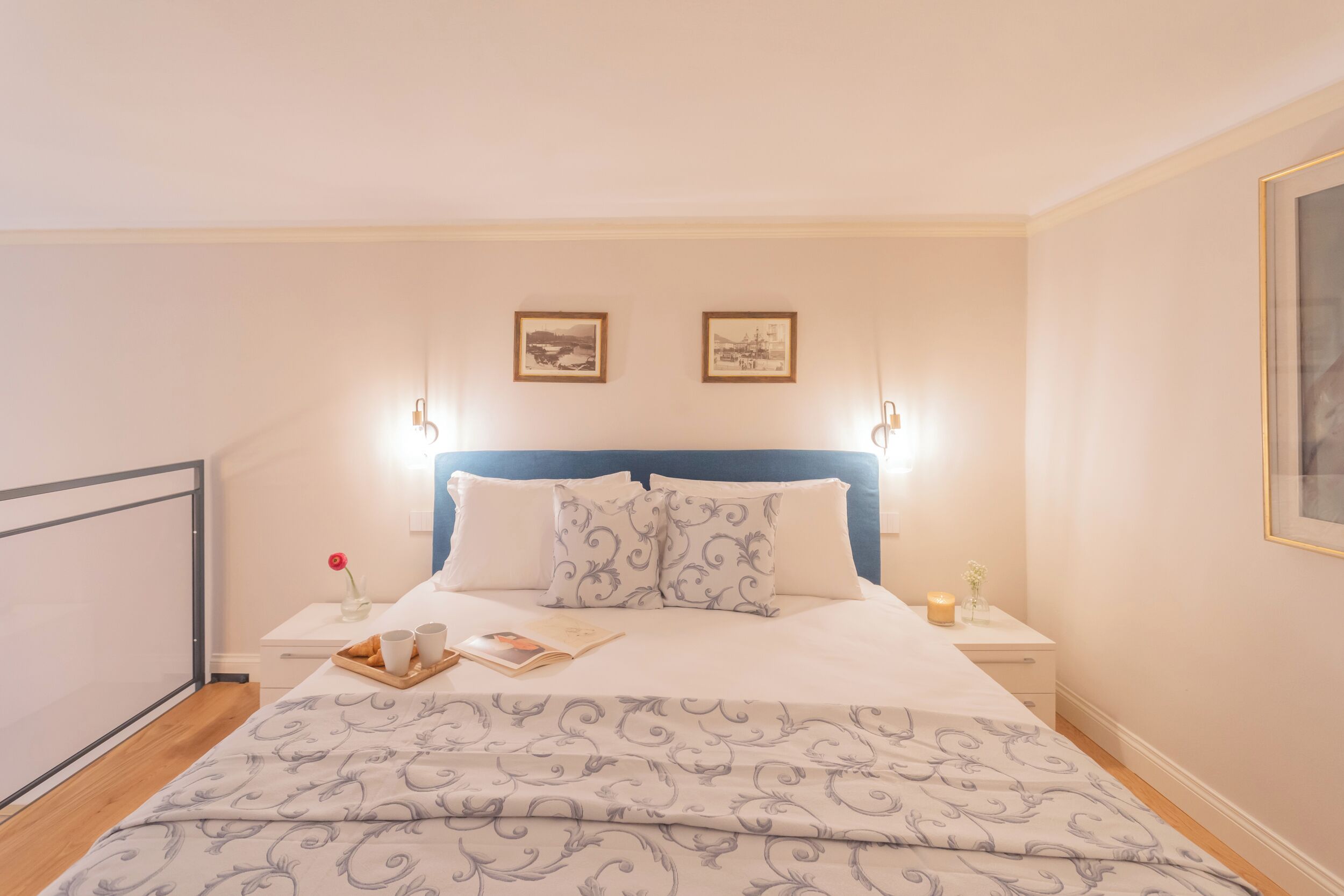 A neatly made bed with a patterned bedspread, two bedside tables with lamps, and two framed pictures on the wall.
