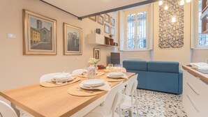 A dining area with a wooden table set for four, white chairs, and a blue sofa. - Cinque Giornate 70 Suites by Rent all Como (Como)