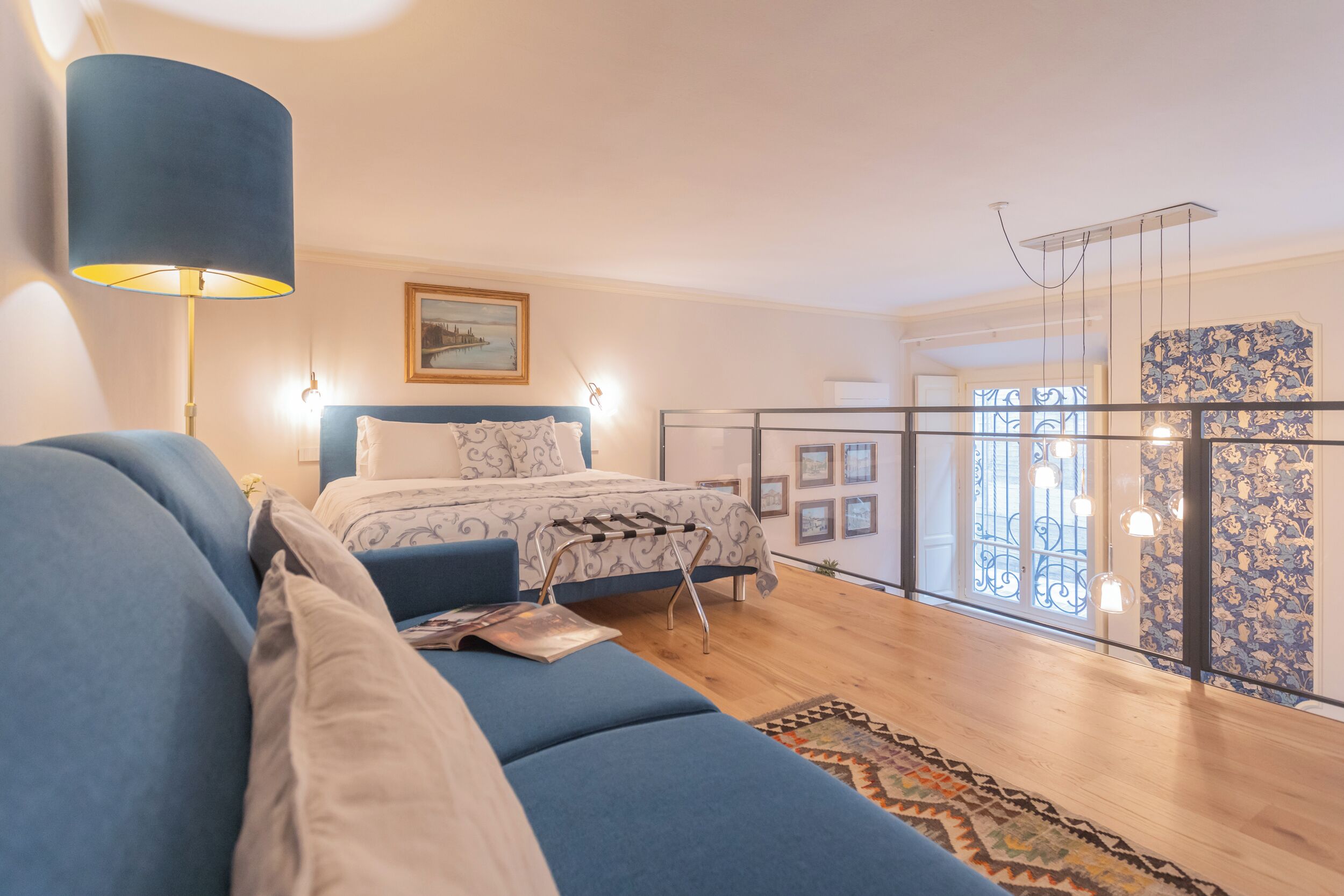 A bedroom with a bed, a blue sofa, a patterned rug, and a view through a glass door.