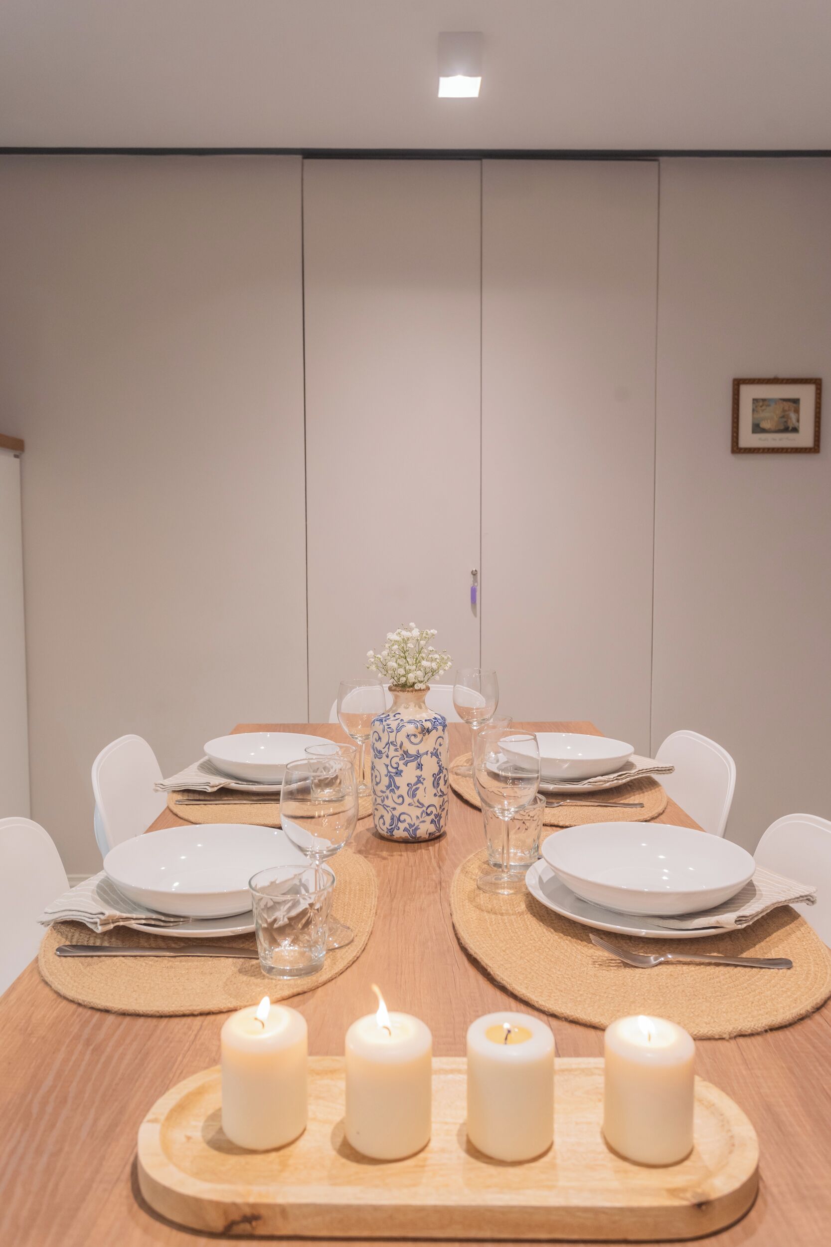 Une table à manger dressée avec des assiettes, des verres et des bougies, et un vase de fleurs placé au centre.