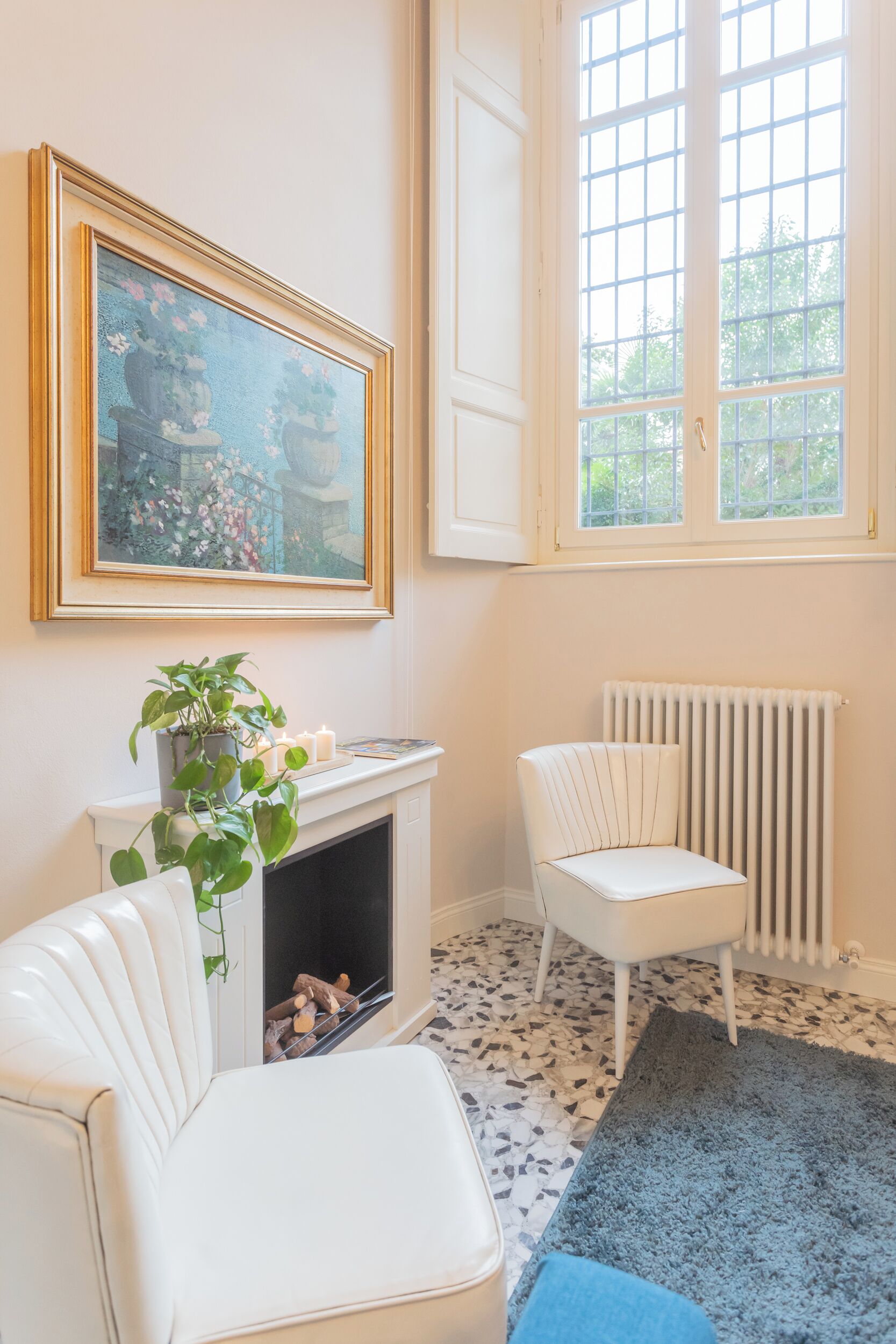 Une pièce avec une cheminée, un fauteuil blanc, un tapis bleu et une fenêtre donnant sur un paysage verdoyant.