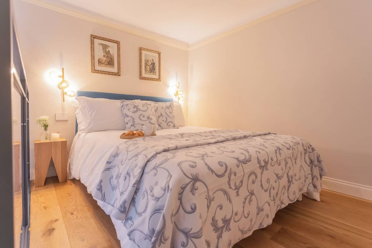 Un dormitorio con cama, mesitas de noche e iluminación en la pared.