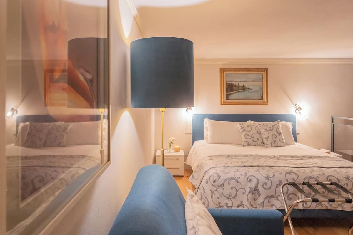 Una habitación de hotel con cama, mesita de noche, lámpara y un cuadro en la pared.