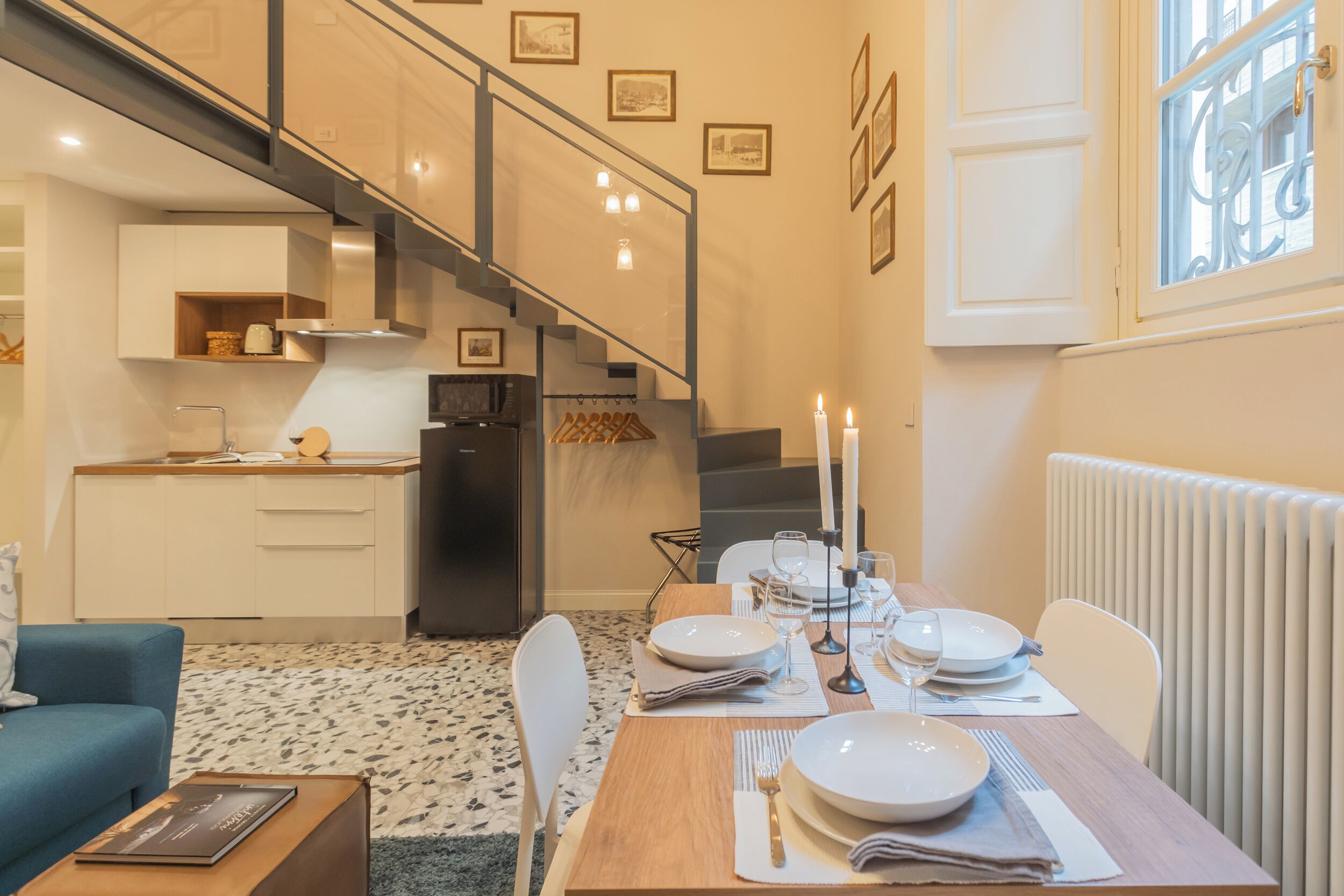 A modern kitchen with a built-in stove, a dining area with a table set for four, and a staircase leading to an upper level.