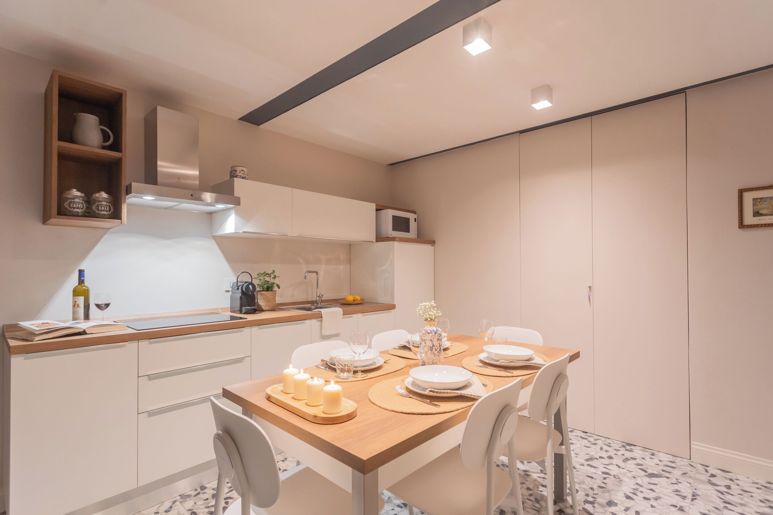 Una cocina moderna con armarios blancos, encimera de madera y una mesa de comedor preparada para cuatro personas, con velas.