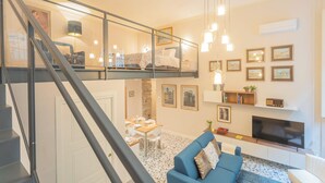A modern living room with a blue sofa, a dining area with a table set for four, and a TV mounted on the wall. - Cinque Giornate 70 Suites by Rent all Como (Como)
