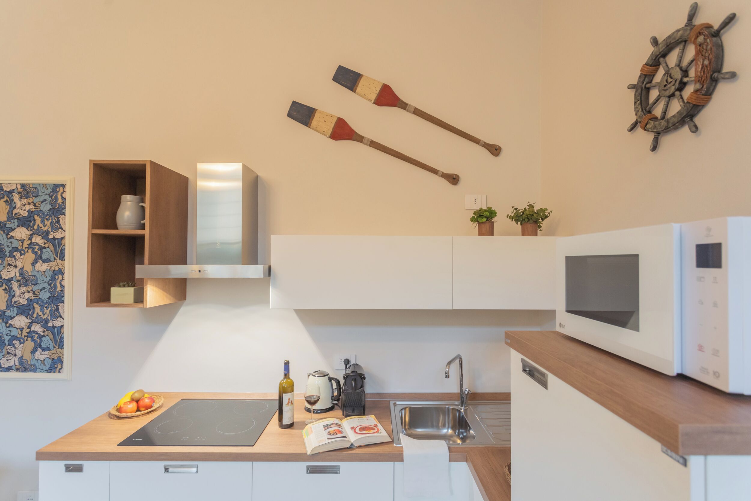 Eine moderne Küche mit Holzarbeitsplatte, einer eingebauten Mikrowelle, einem Wasserkocher und einem Kochtopf auf dem Herd. Zwei hölzerne Pfannenwender hängen an der Wand und ein Blumentopf steht auf der Arbeitsplatte.