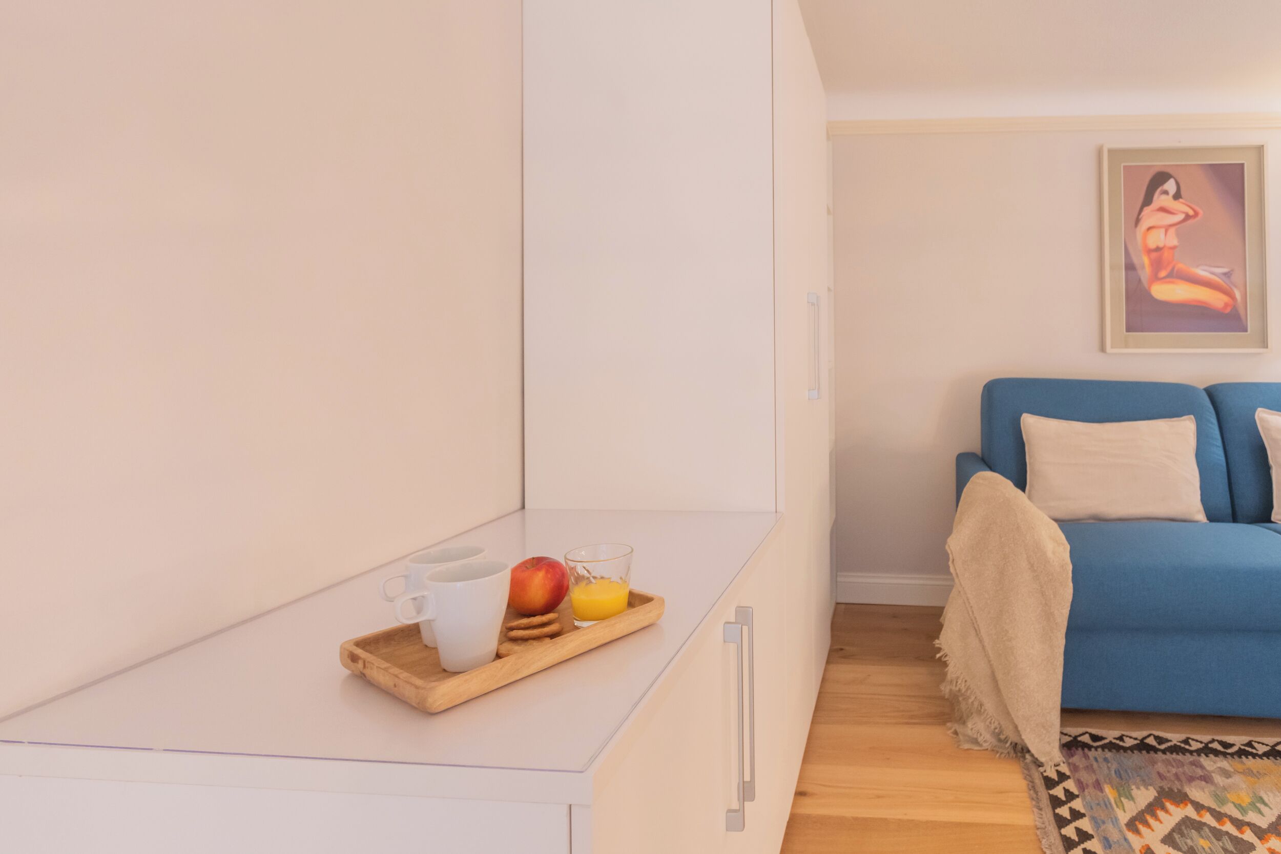 Un soggiorno moderno con un divano blu, un piccolo tavolino con un vassoio pieno di frutta e una tazza, e un quadro appeso al muro.