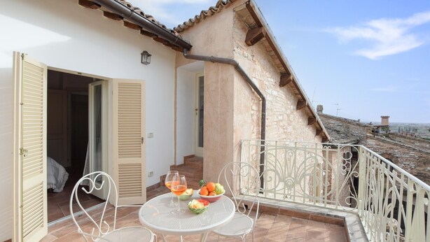 A balcony with a table set for two, a chair, and a view of the countryside. - Stunning home in Spello with WiFi (Spello)