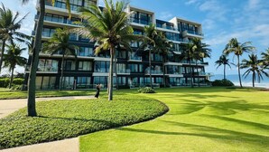 A modern hotel with multiple floors, large windows, and a well-maintained lawn with palm trees.
