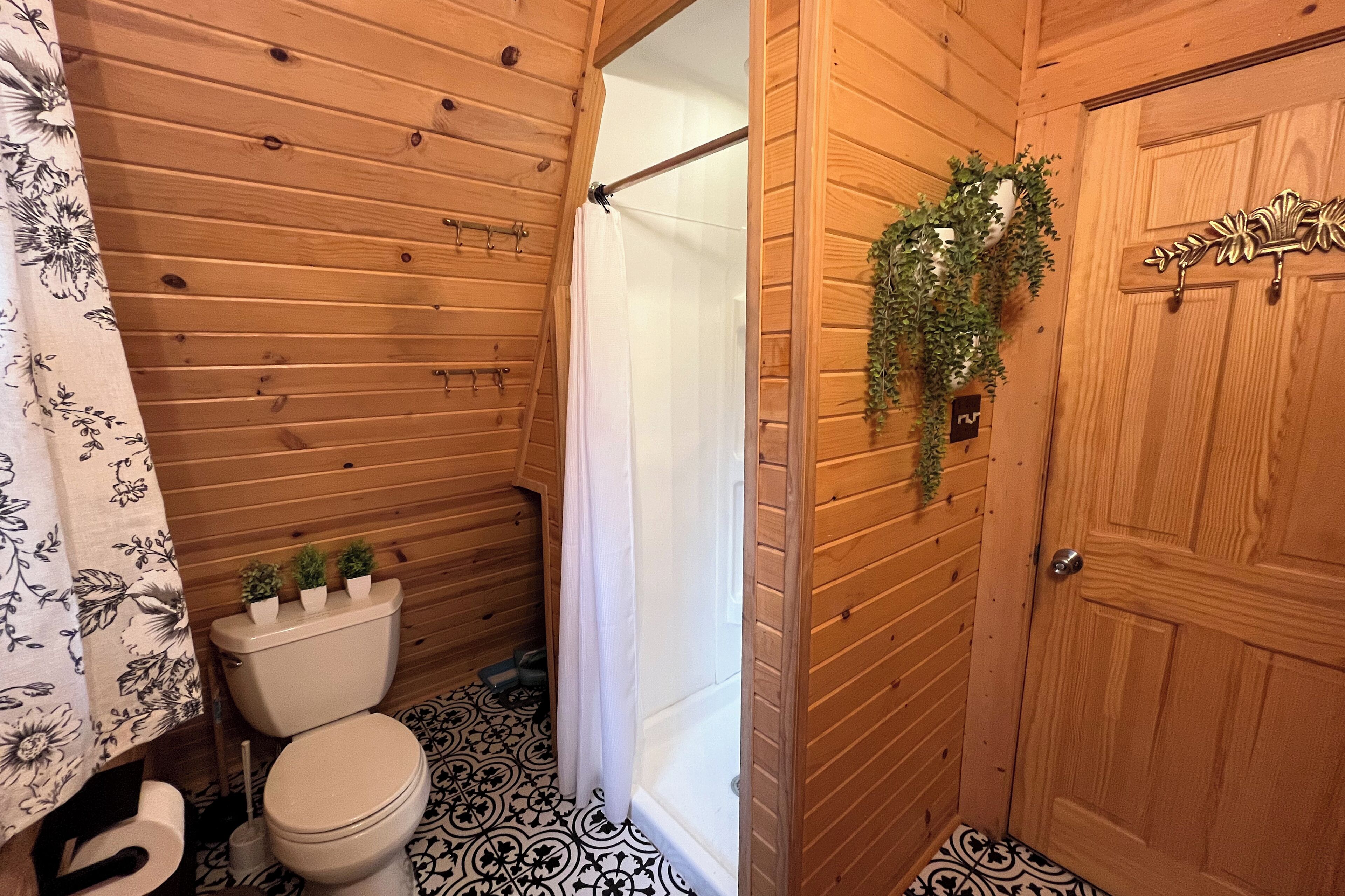 Ein Badezimmer mit Holzpaneelen, einer Toilette, einer Duschkabine und einer Tür mit dekorativer Metallbeschlag.