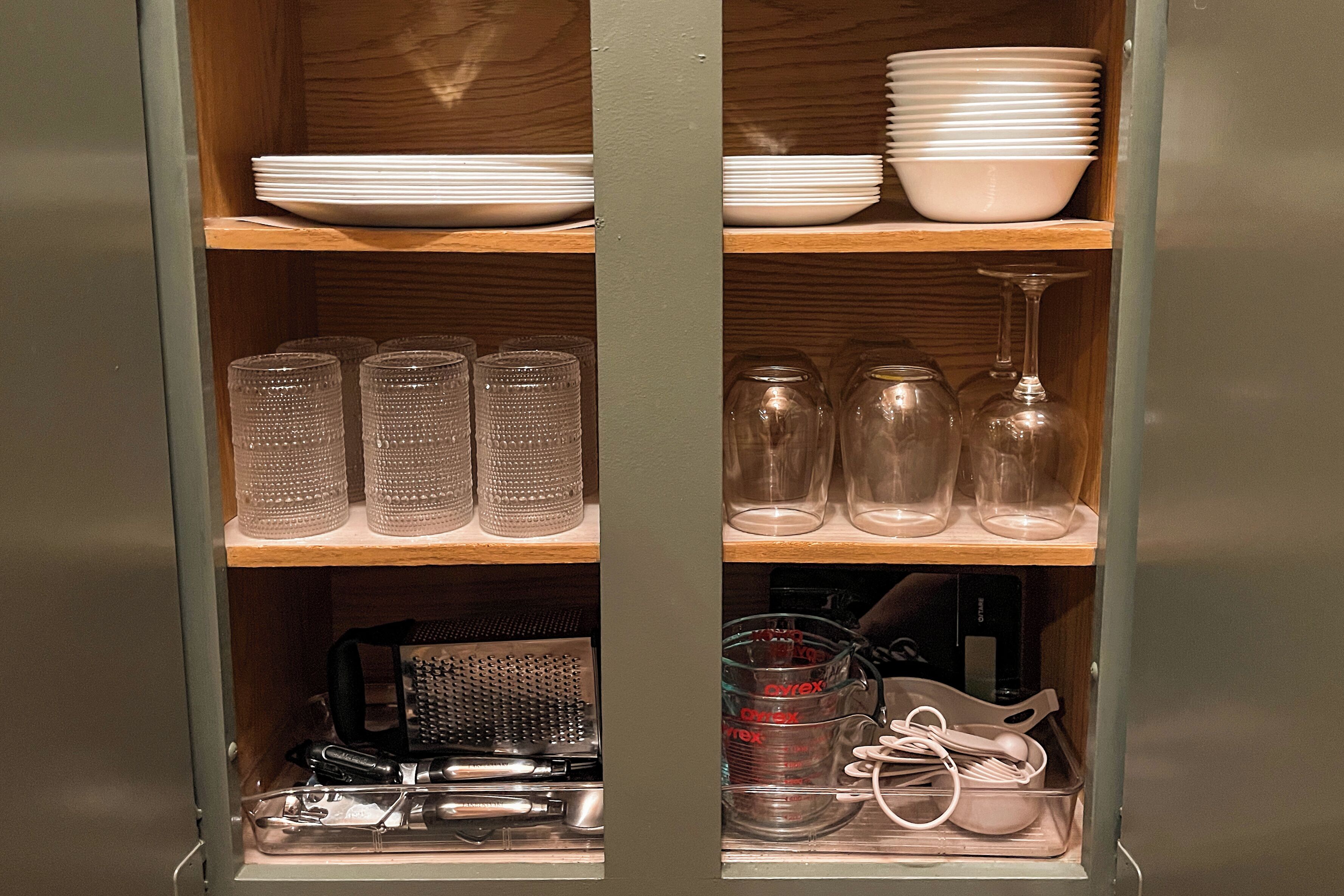 A kitchen cabinet with shelves holding plates, glasses, and kitchen utensils.