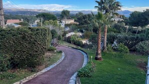 A curved pathway in a residential area with houses, palm trees, and a mountainous backdrop. - TOP VILLA PALOMA ANTIBES Vue Mer, Montagne, FIBRE, CLIME, POOL (Antibes)