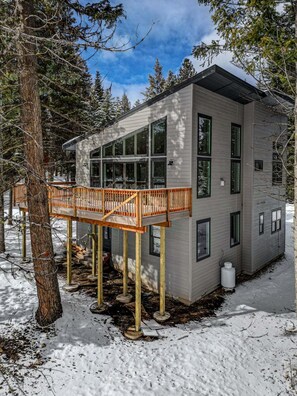 Um edifício moderno com grandes janelas, um deck de madeira e um ambiente coberto de neve.