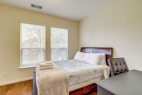 A bedroom with a bed, a desk, and two windows with blinds.