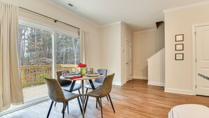 Un coin repas avec une table dressée pour quatre personnes, une terrasse en bois à l’extérieur et un escalier menant à un autre étage.