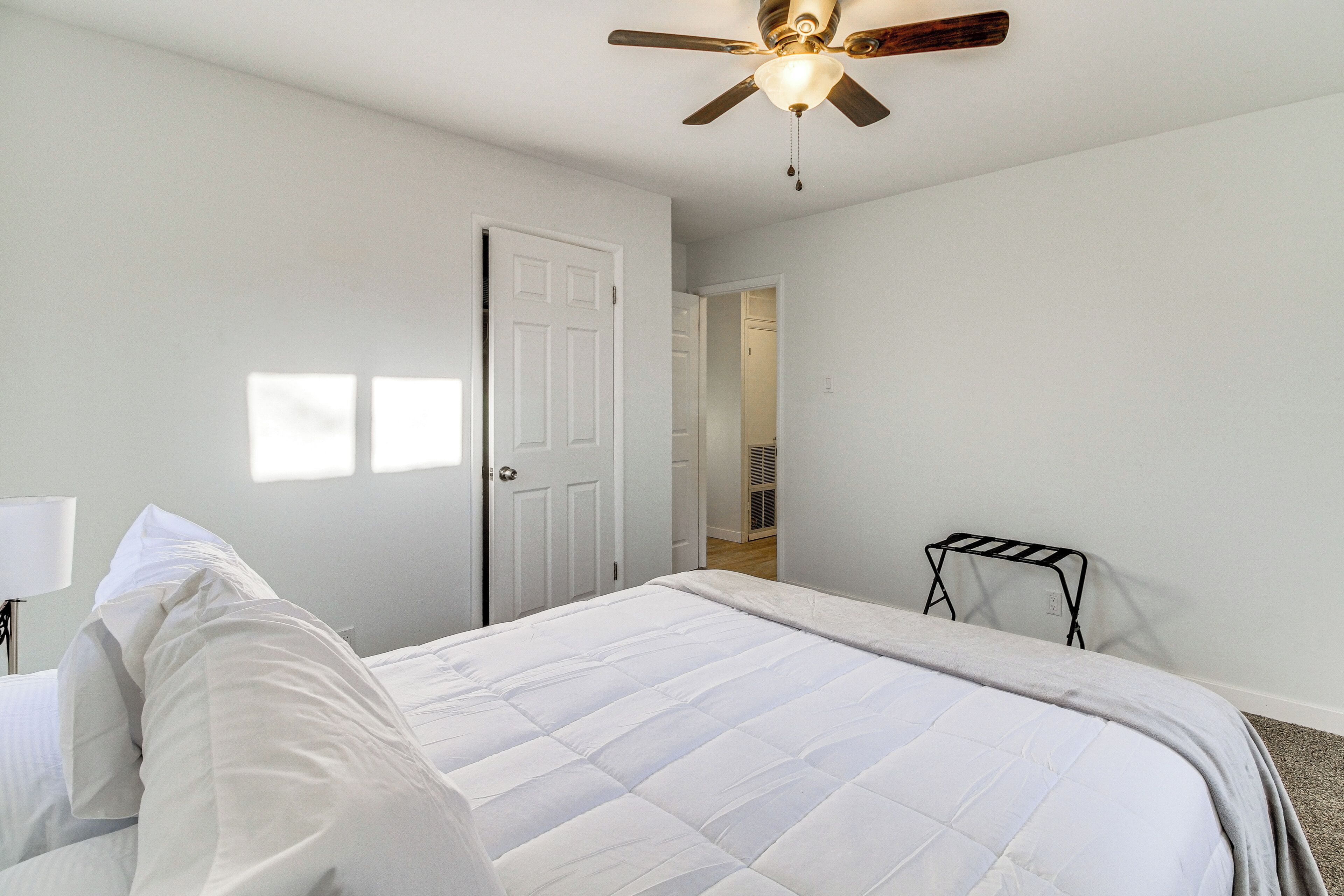 A bedroom with a bed, a ceiling fan, and a door leading to another room.