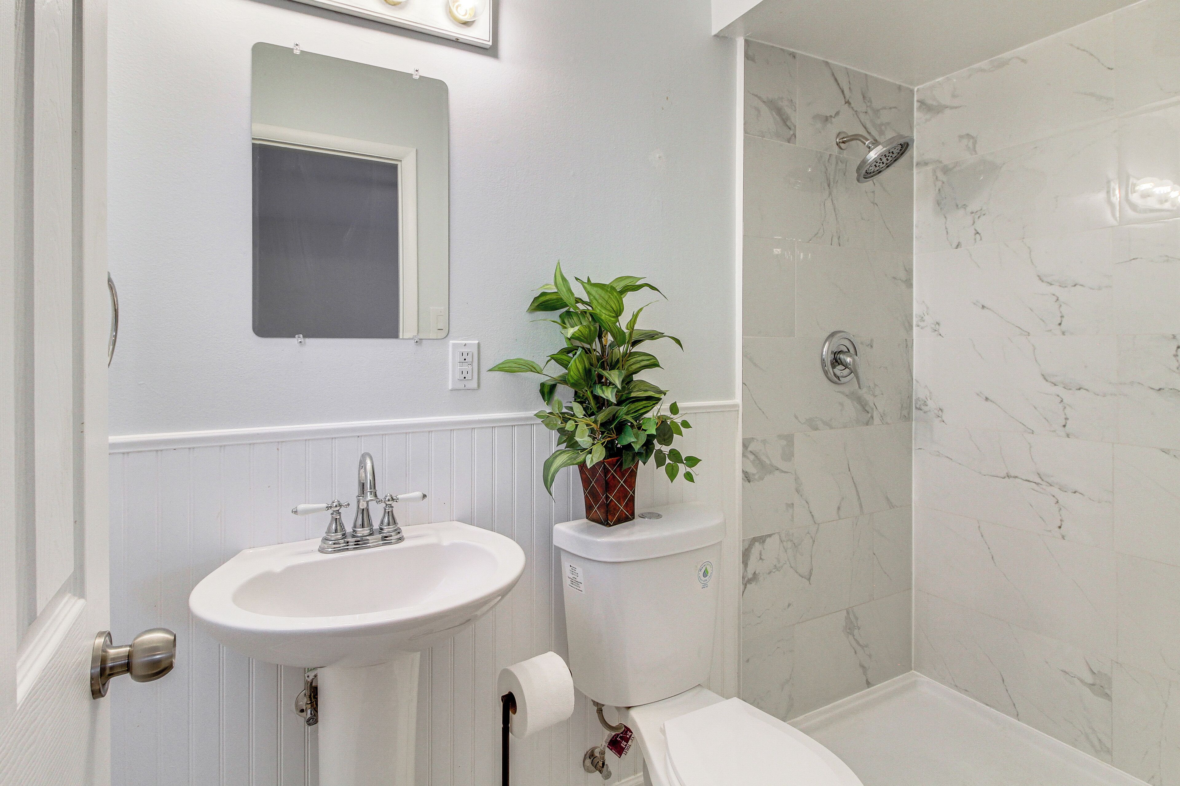 A bathroom with a white sink, a toilet, a shower, and a potted plant.