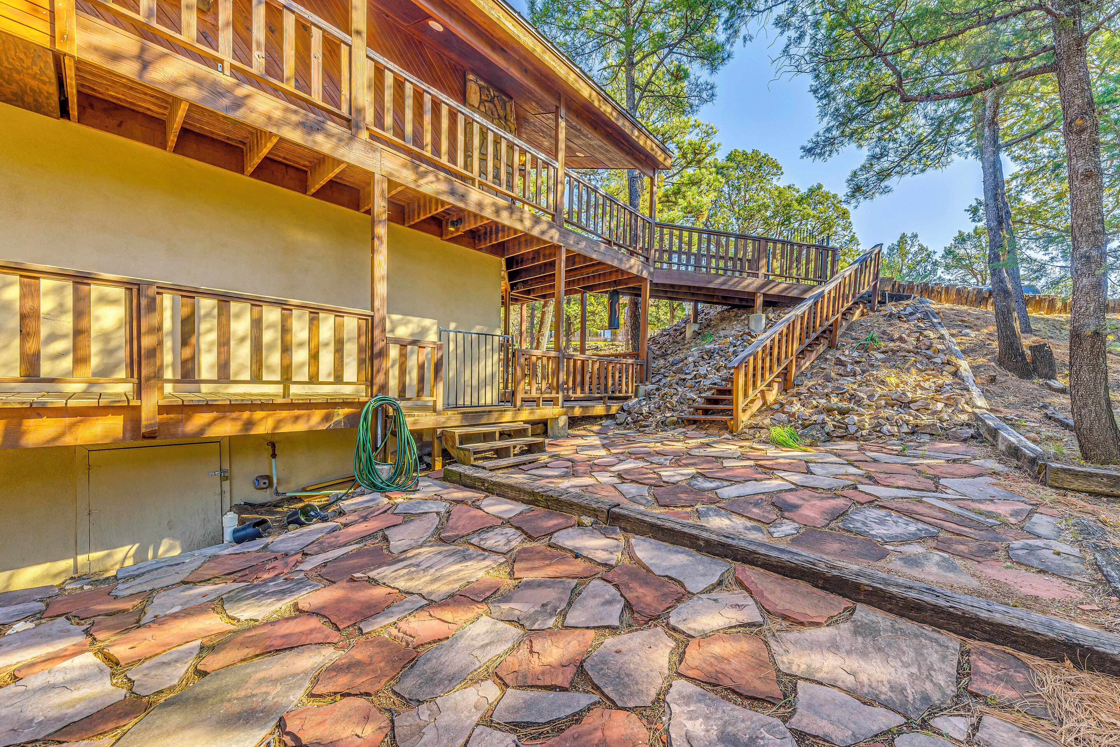 A wooden cabin with a stone-paved patio, wooden deck, and a staircase leading to a second level.
