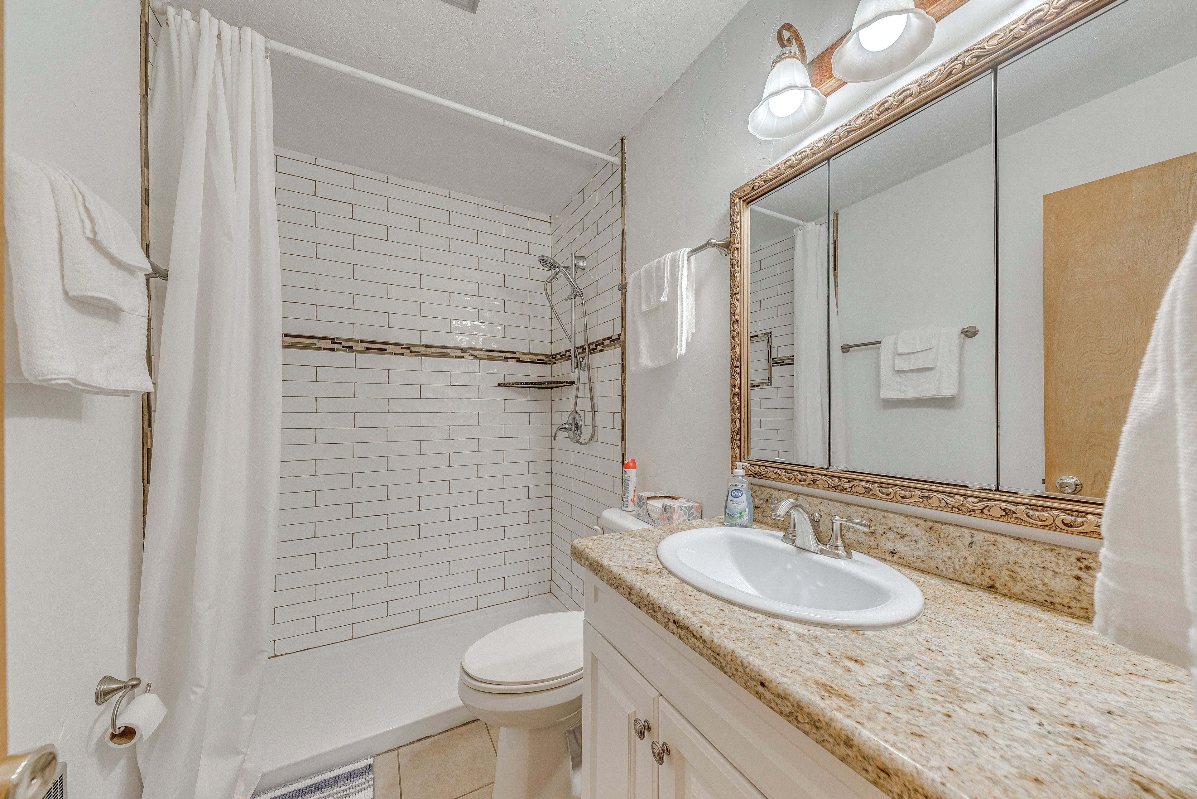 Un baño con inodoro blanco, ducha con puerta de cristal, lavabo con espejo y toallero.