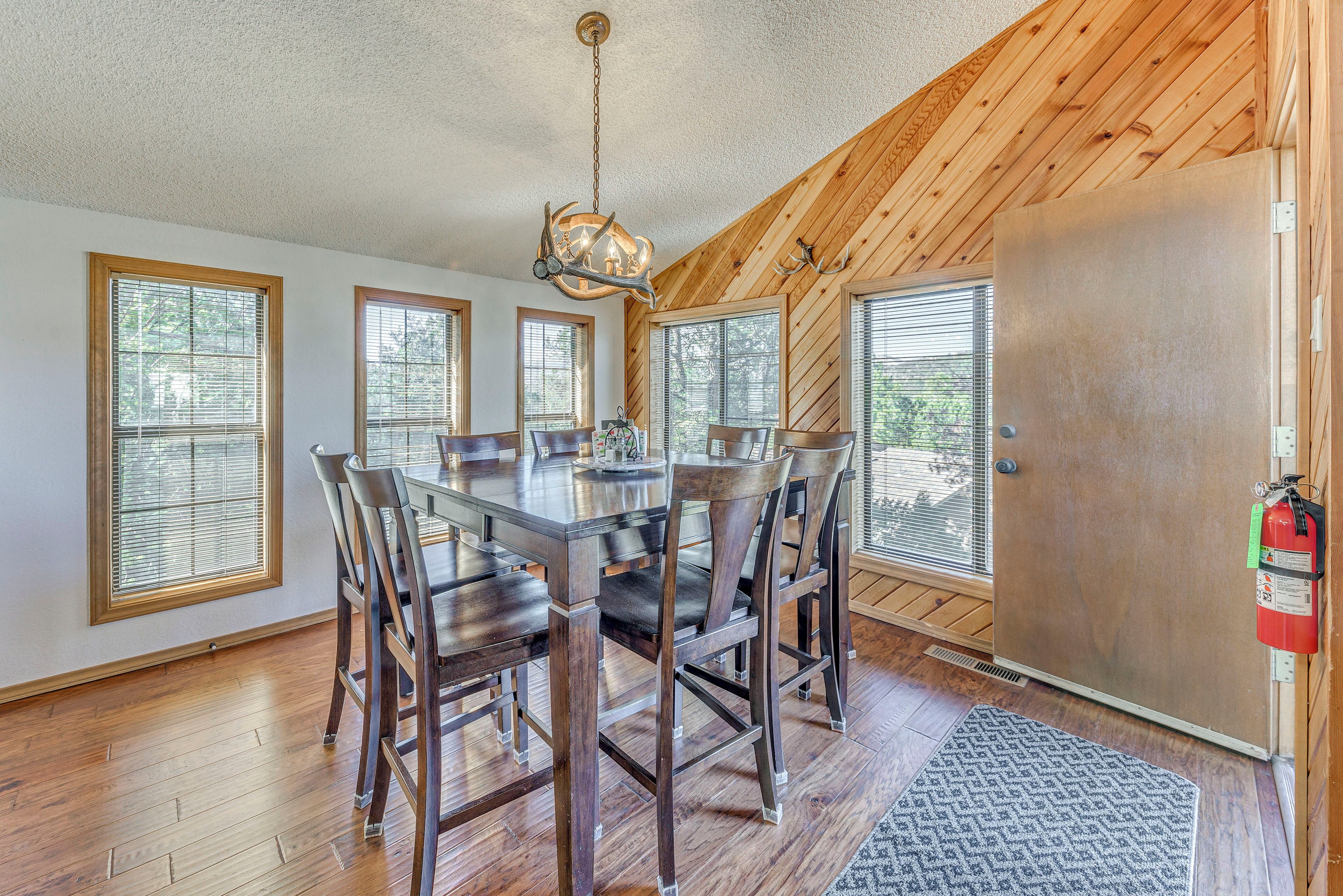 A dining area with a wooden table and chairs, large windows, and a fire extinguisher on the wall.