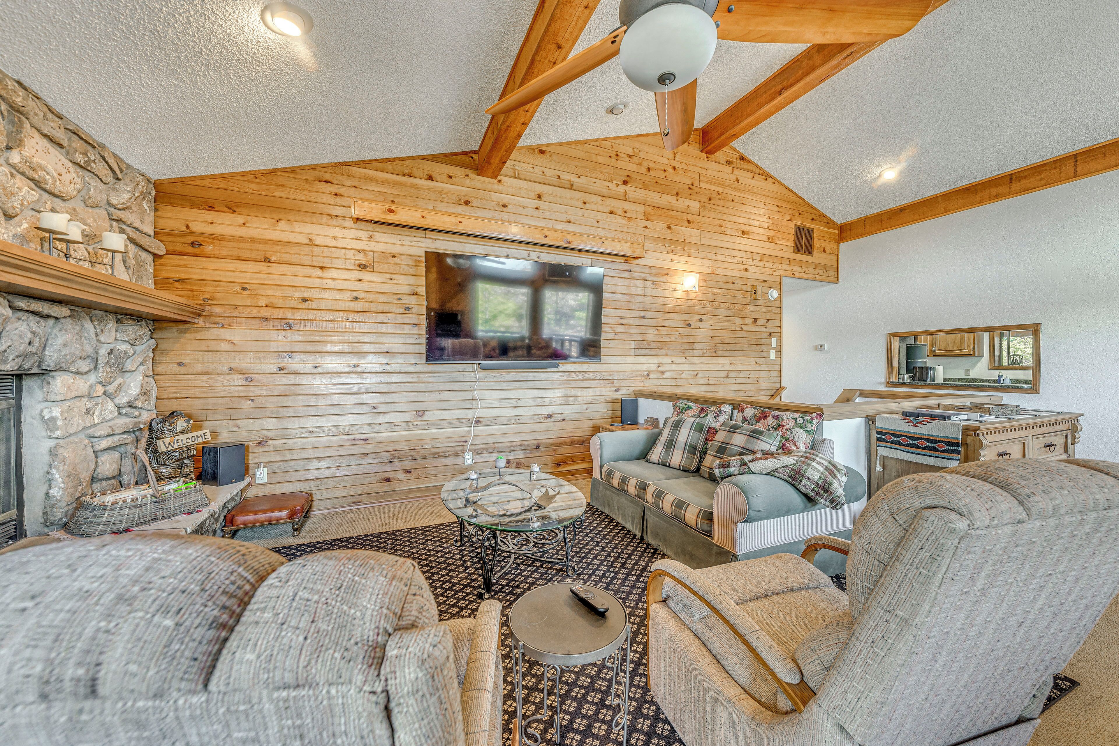 A cozy log cabin interior with a stone fireplace, wooden walls, a television, and comfortable seating.
