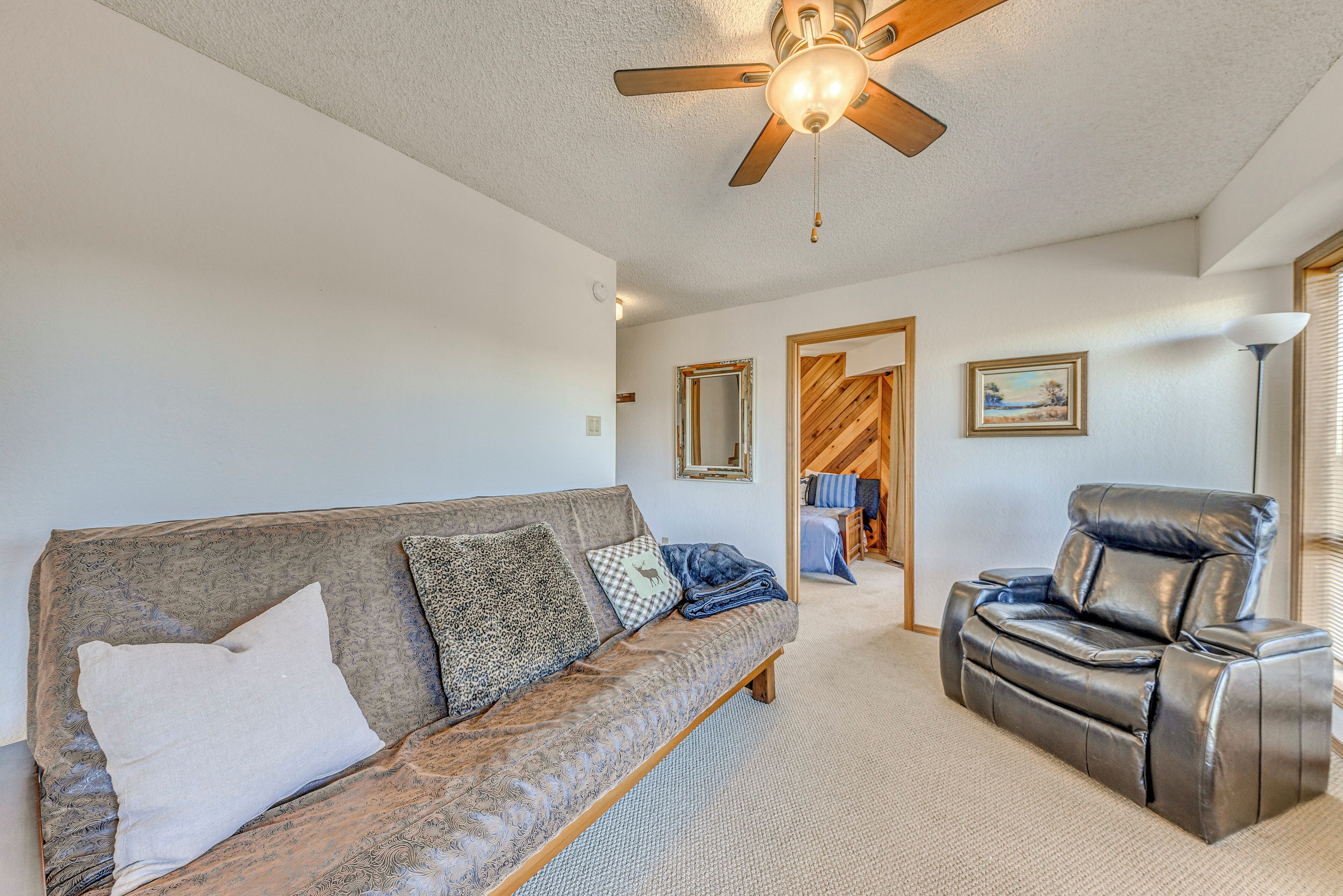 A living room with a sofa, a recliner, a ceiling fan, and a door leading to another room.