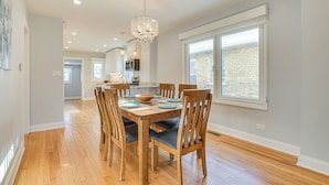 A dining area with a wooden table and chairs, a chandelier, and a view of the outside through a large window. - 2 Mi to Northwestern: Updated Home w/ Game Room! (Evanston)