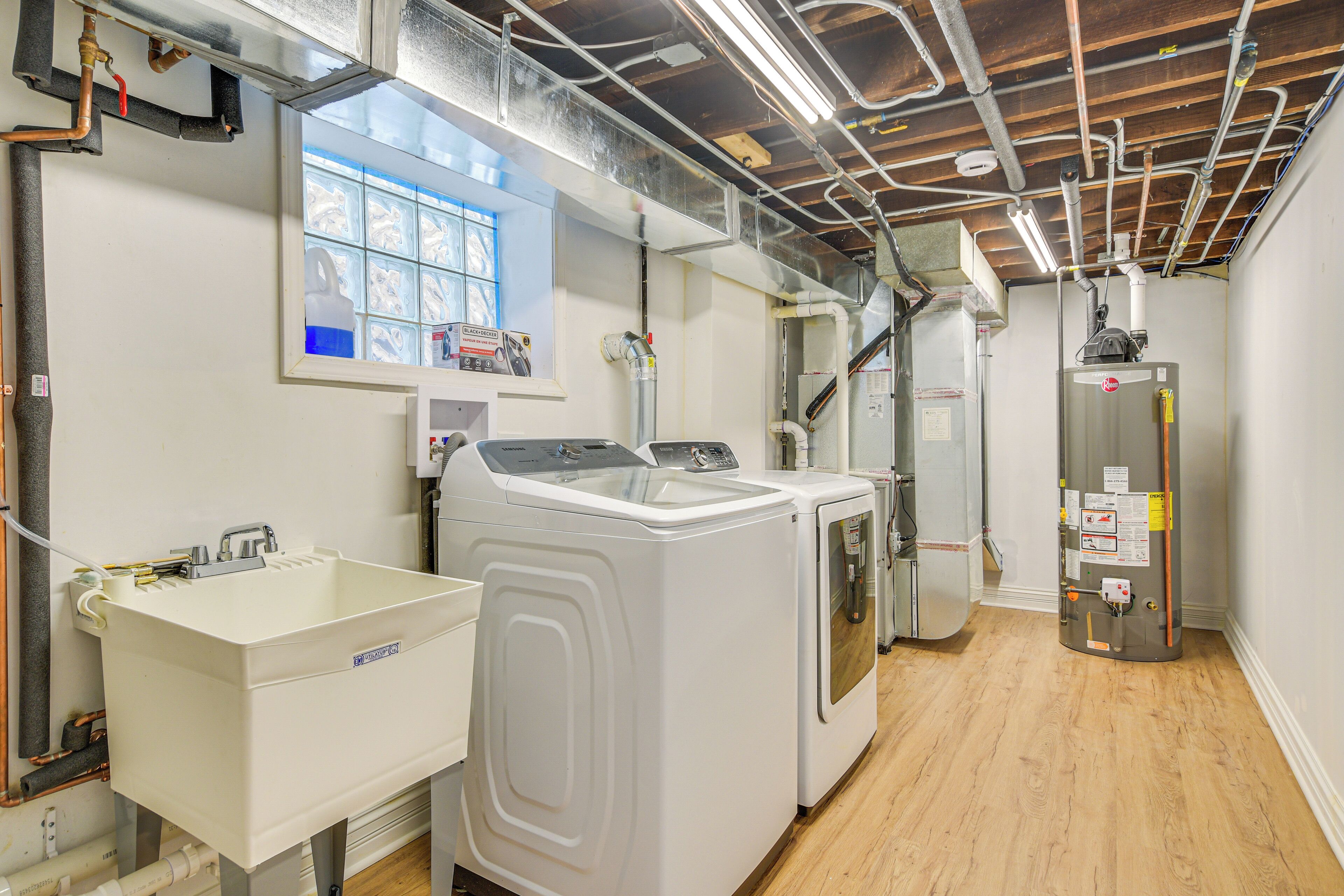 A laundry room with a sink, washing machine, and dryer, with visible pipes and a window above the sink.