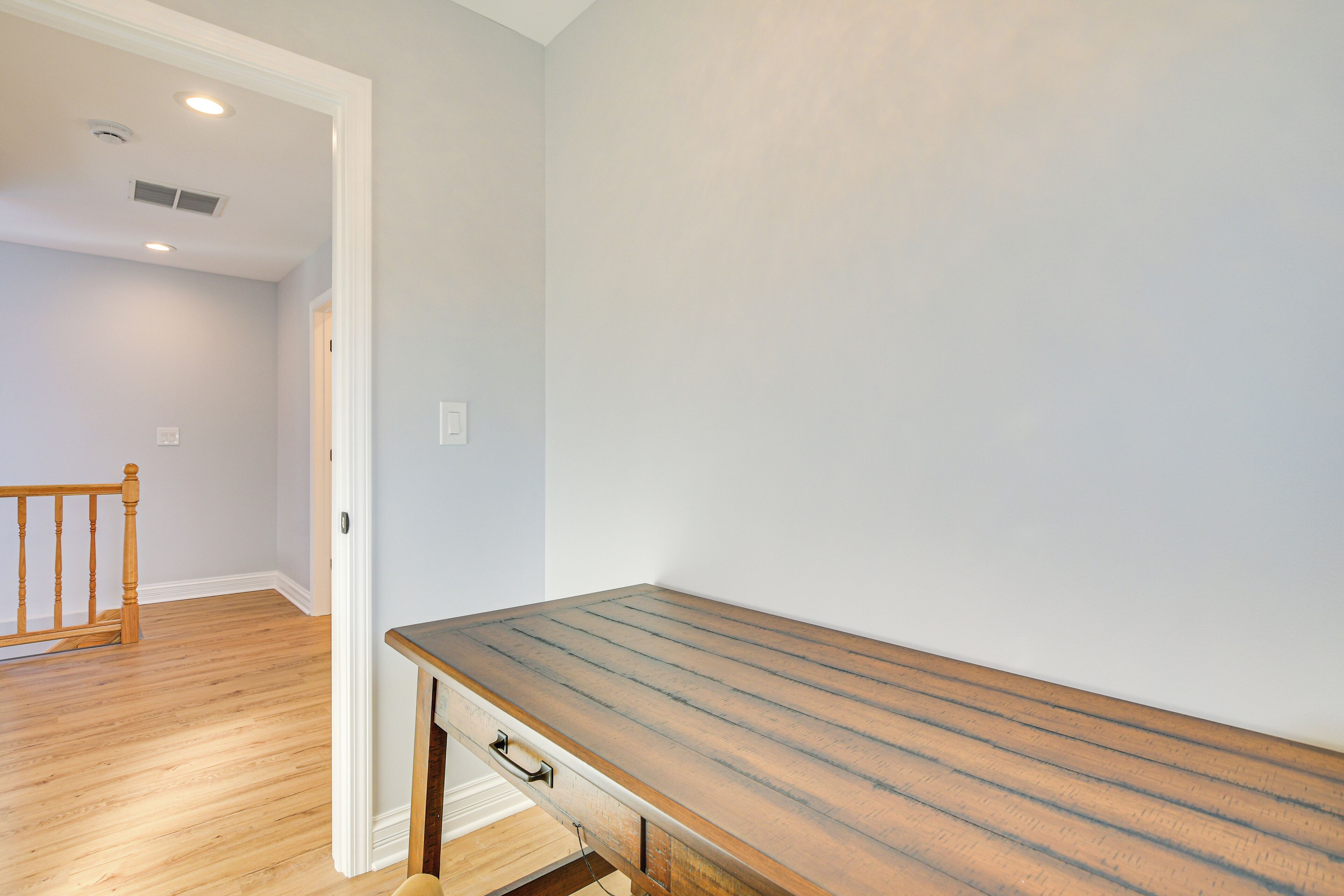 Une pièce avec un plancher en bois, un banc en bois, une porte blanche et un mur blanc.