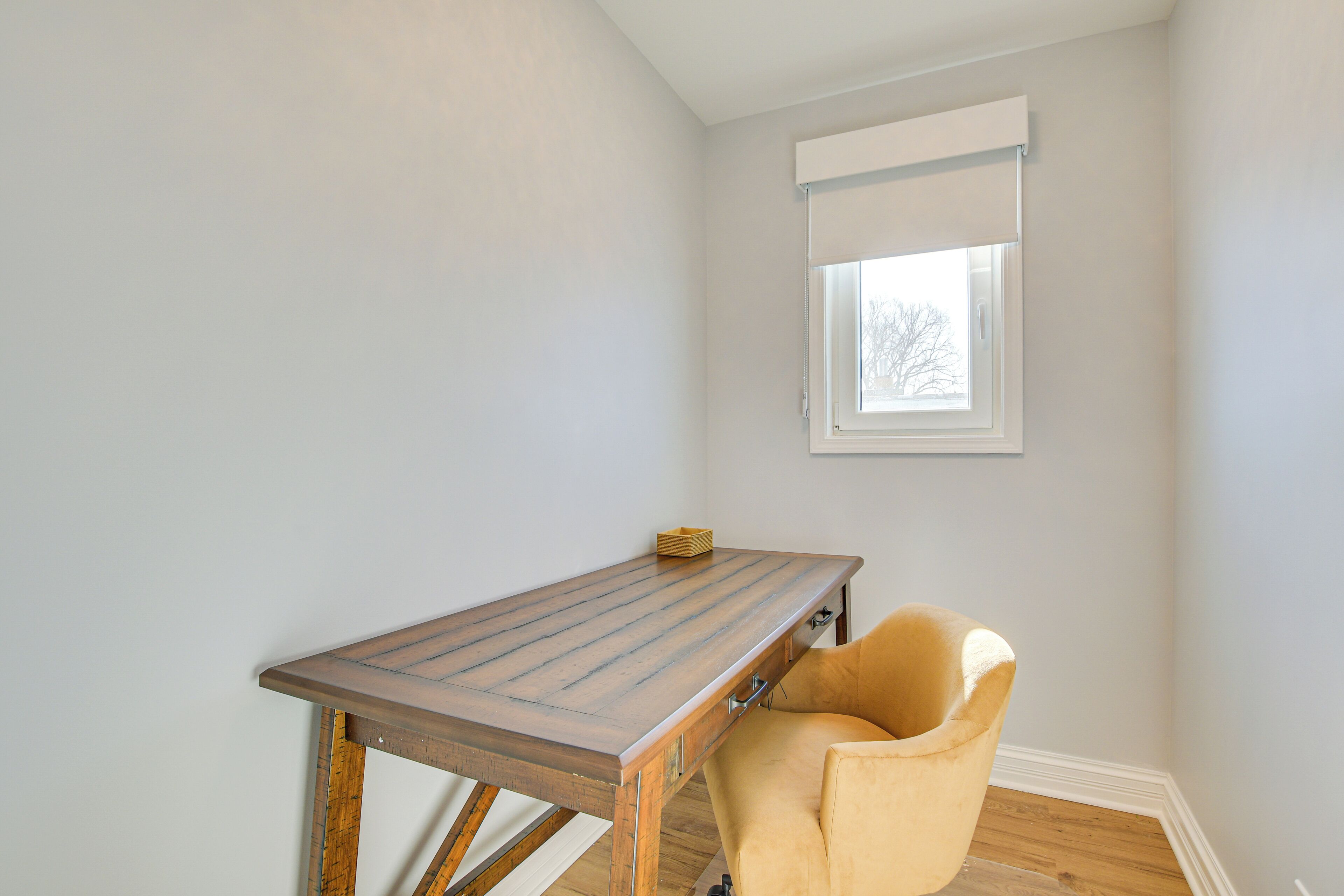 A room with a wooden table, a yellow chair, a window with blinds, and a white wall.