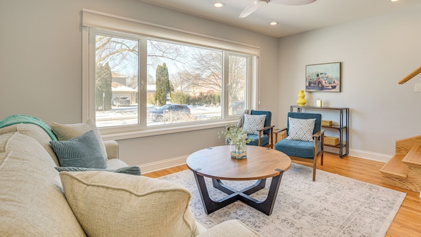 A living room with a large window, a ceiling fan, a round coffee table, and a blue armchair. - 2 Mi to Northwestern: Updated Home w/ Game Room! (Evanston)