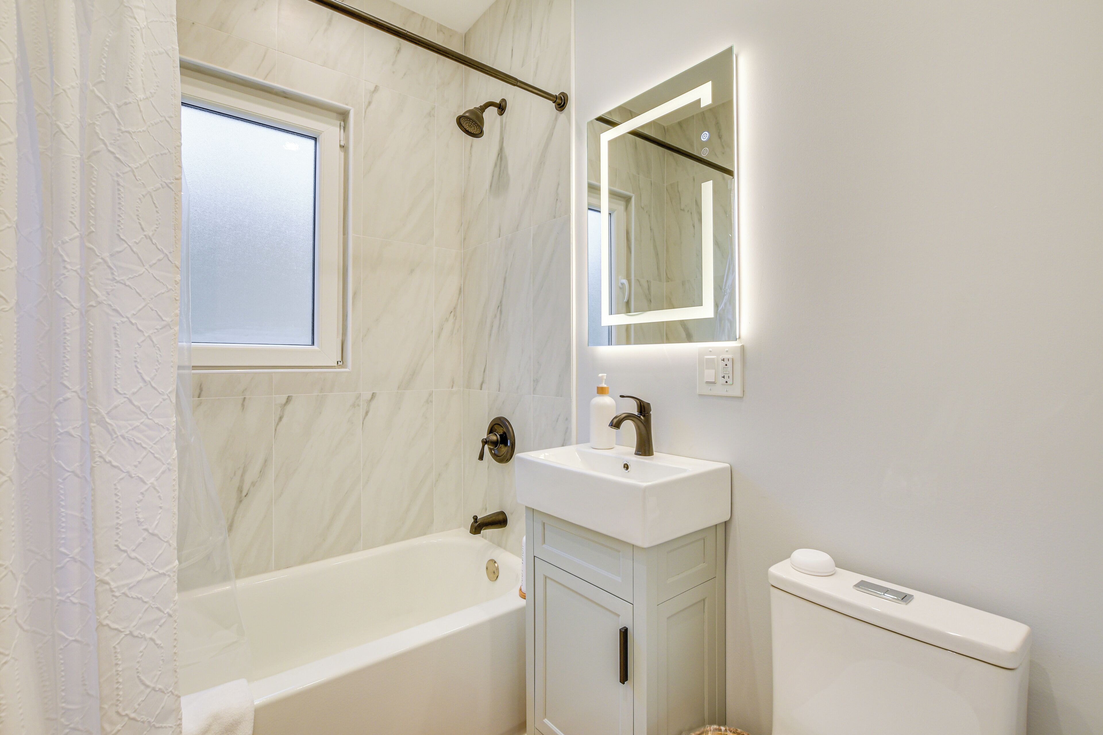 A bathroom with a bathtub, a sink, a toilet, and a window.