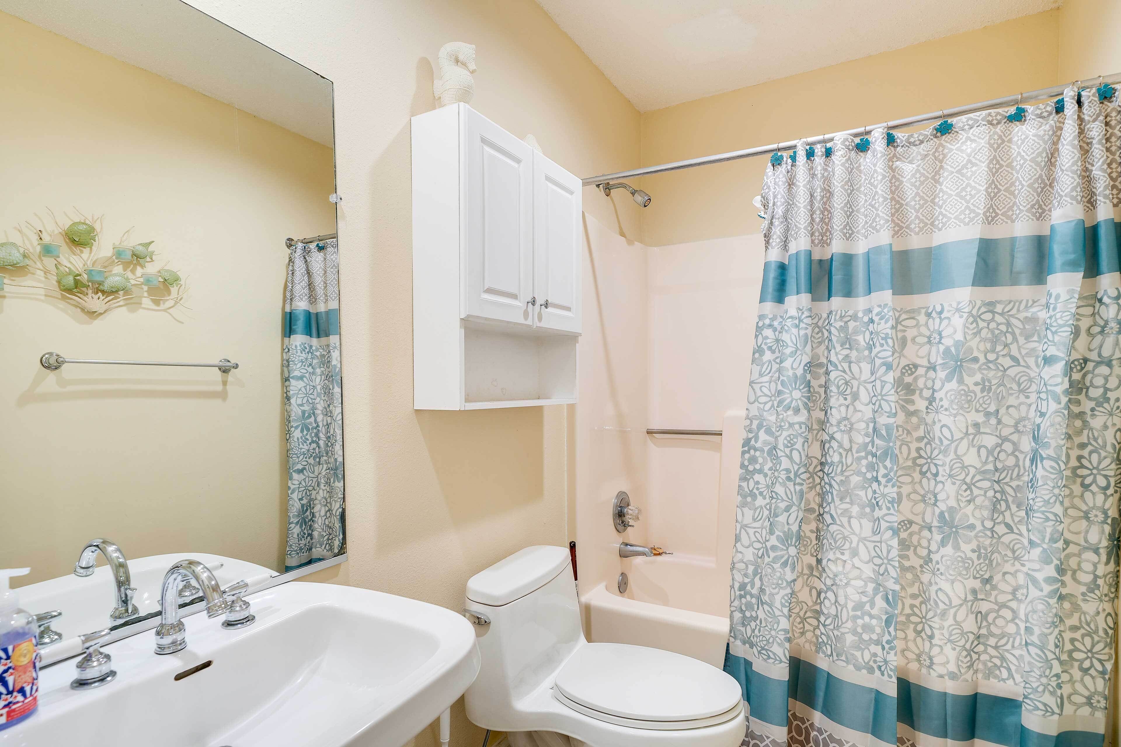 A bathroom with a white sink, two faucets, a toilet, and a shower curtain with a floral pattern.