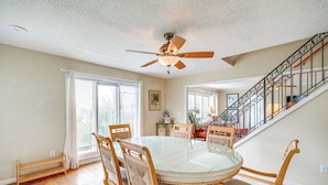 A dining area with a glass-top table, wooden chairs, and a ceiling fan. - Rooftop Deck & Hot Tub: Outer Banks Family Getaway (Salvo)