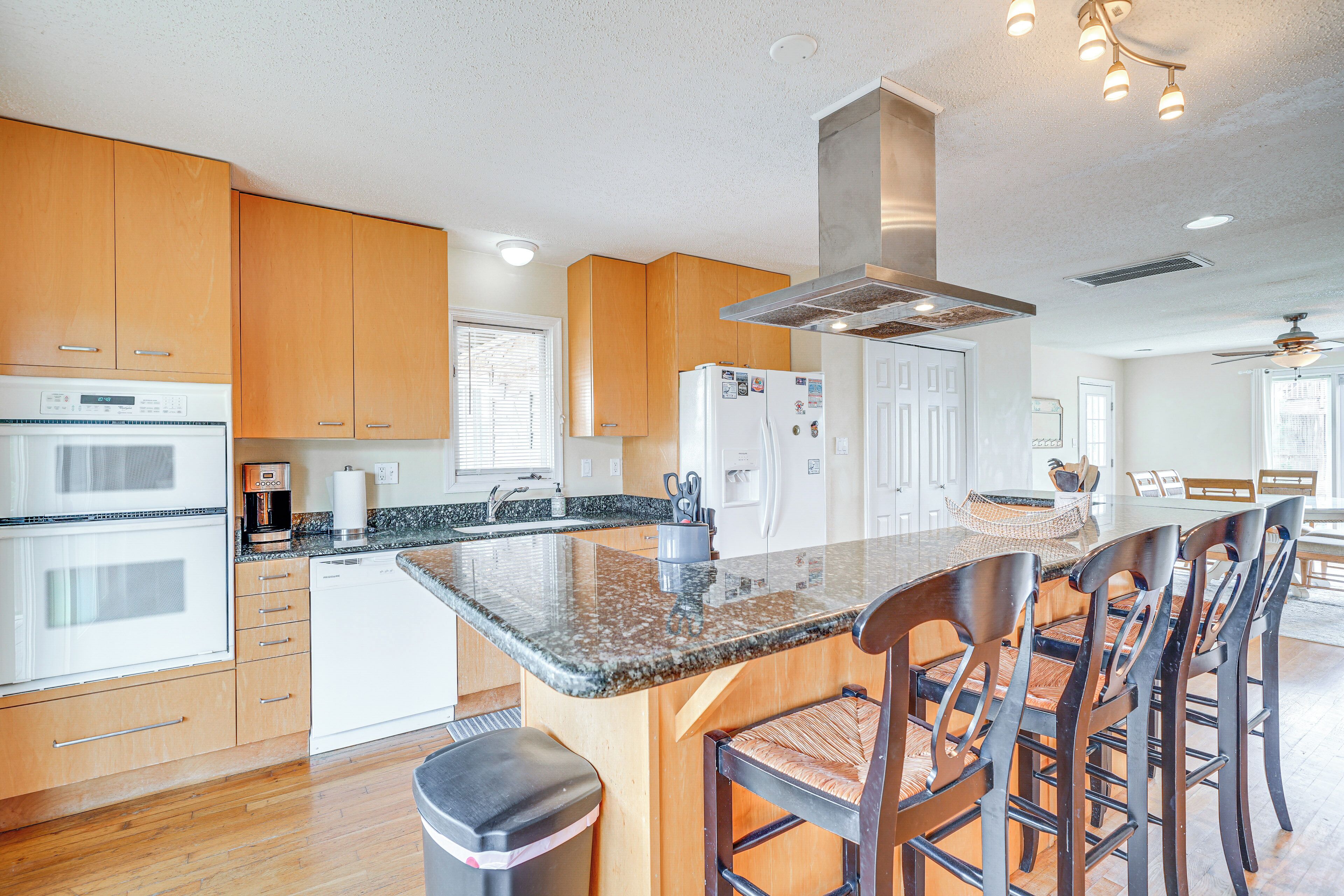 A modern kitchen with wooden cabinets, a granite countertop, a built-in oven, and a central island with bar stools.