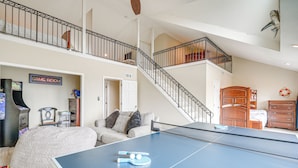 A spacious living area with a ping pong table, a couch, and a staircase leading to an upper level. - Rooftop Deck & Hot Tub: Outer Banks Family Getaway (Salvo)