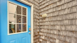 A blue door with a window and a light fixture on the exterior wall. - Rooftop Deck & Hot Tub: Outer Banks Family Getaway (Salvo)