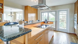 A modern kitchen with granite countertops, wooden cabinets, a stainless steel range hood, and a large window providing a view of the outdoors. - Rooftop Deck & Hot Tub: Outer Banks Family Getaway (Salvo)