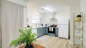 Et moderne køkken med lysegrå skabe, et rustfrit stål emfang, et hvidt køleskab og et træspisebord med en vase med grønne planter.