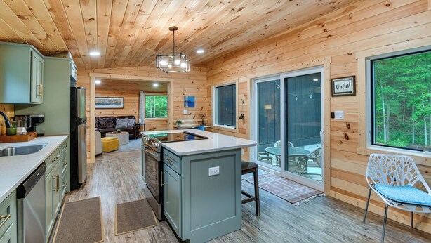 A cabin interior with a kitchen, dining area, and large windows. - Explore Lakes & Beaches! Creekside Glen Arbor Home (Glen Arbor)